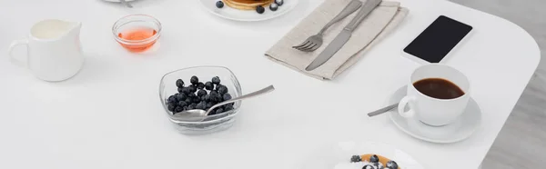 Високий кут зору смачних млинців біля мобільного телефону та кави на столі, банер — стокове фото