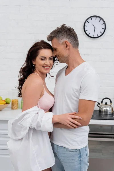 Homme étreignant femme séduisante en soutien-gorge et chemise dans la cuisine — Photo de stock