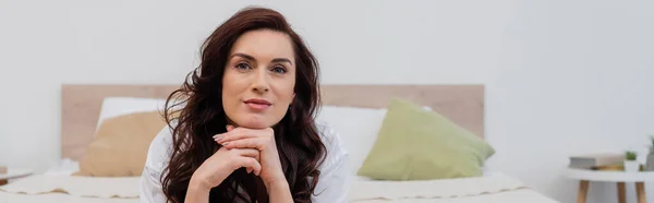 Woman in white shirt looking at camera while lying on bed, banner — Stock Photo