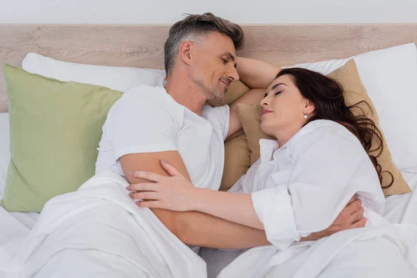 Smiling man hugging sleeping wife in shirt on bed — Stock Photo
