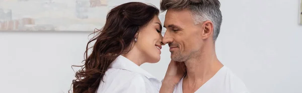 Улыбающаяся брюнетка в рубашке целует мужа дома, баннер — стоковое фото