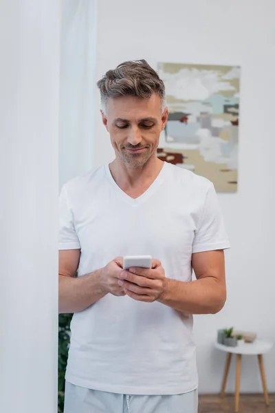 Sorrindo homem de pijama usando smartphone em casa — Fotografia de Stock