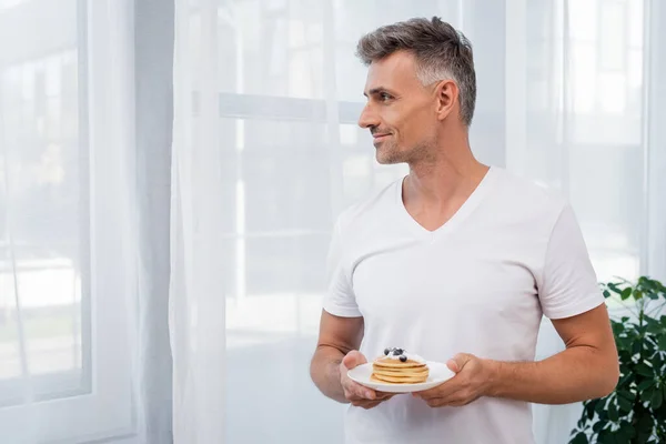 Side view of man holding pancakes with blueberries at home — Stock Photo