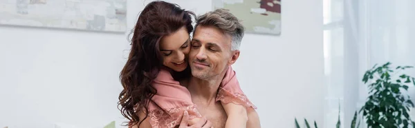 Positive woman in silk robe embracing shirtless husband at home, banner — Stock Photo