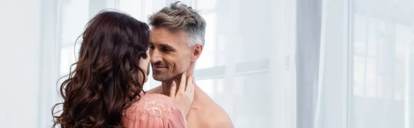 Woman in silk robe touching nick of shirtless husband at home, banner — Stock Photo