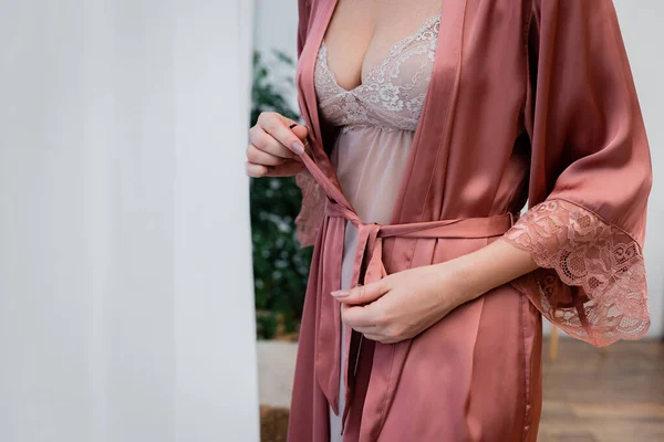 Vue recadrée de la femme en nuisette attachant robe de soie à la maison — Photo de stock
