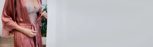 Cropped view of woman in nightie tying satin robe at home, banner — Stock Photo