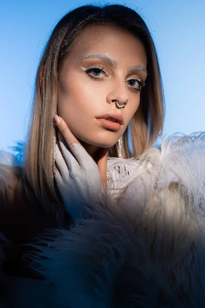 Jeune femme blonde avec des sourcils enneigés et la peau gelée regardant caméra sur bleu — Photo de stock