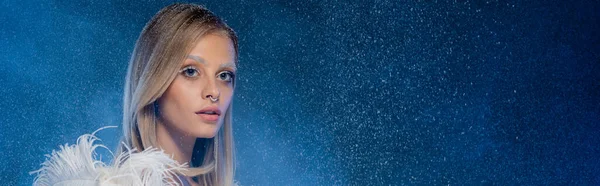 Mujer joven perforada con nieve en el pelo y maquillaje de invierno posando en azul oscuro, pancarta - foto de stock