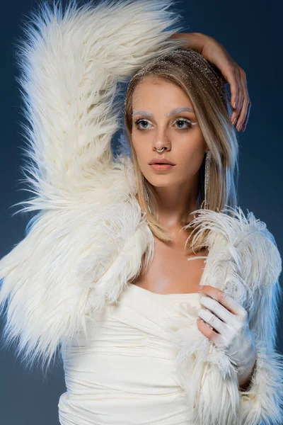 Jeune femme blonde avec des morceaux posant dans une veste blanche en fausse fourrure sur bleu foncé — Photo de stock