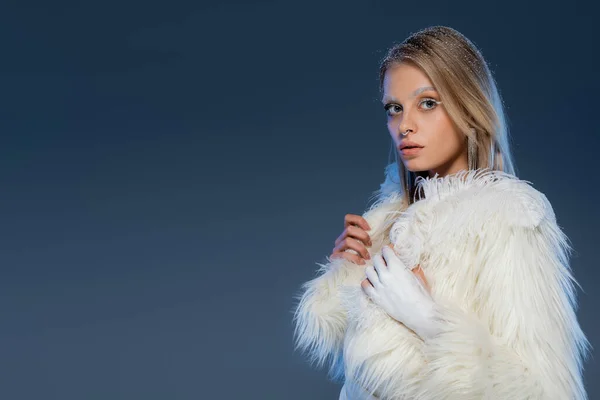 Blonde woman with piecing posing in white faux fur jacket and holding feather on dark blue background — Stock Photo