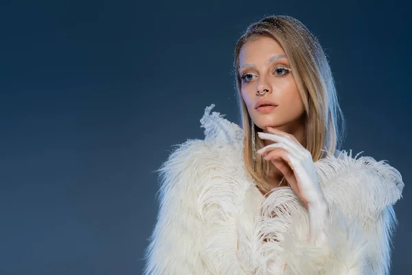 Blonde woman with piecing posing in white faux fur jacket with feathers on dark blue background — Stock Photo