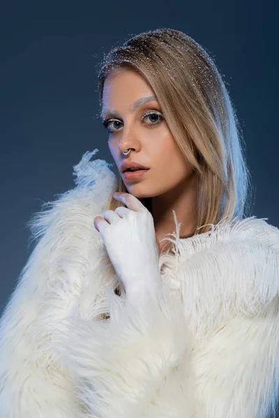 Mujer joven con maquillaje de invierno posando en chaqueta de piel sintética con plumas en azul oscuro - foto de stock