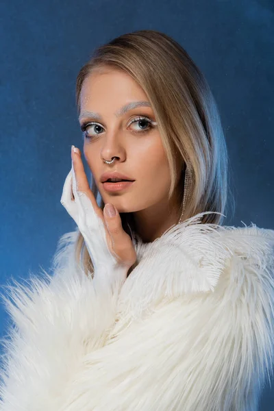 Young pierced woman in winter faux fur jacket posing on dark blue — Stock Photo