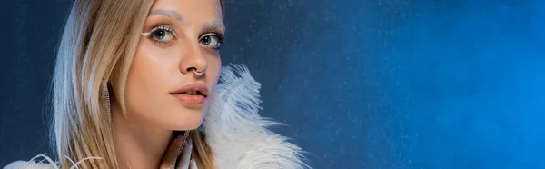 Блондинка з зимовим макіяжем і замороженими бровами позує на темно-синьому фоні, банер — стокове фото