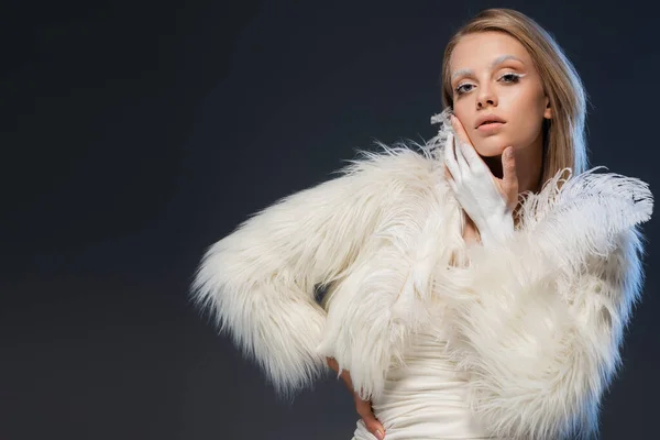 Jeune femme blonde avec un maquillage d'hiver posant en veste blanche en fausse fourrure avec des plumes isolées sur bleu — Photo de stock