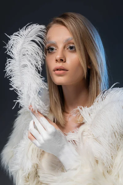 Blonde jeune femme avec le maquillage d'hiver posant en fausse fourrure blanche veste tenant plume isolé sur bleu — Photo de stock