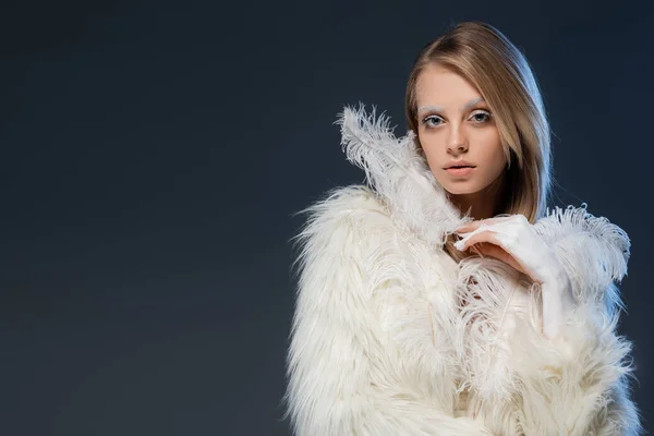 Blonde young woman in faux fur jacket posing with feather isolated on blue — Stock Photo