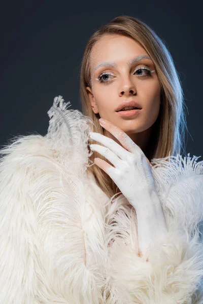 Pretty young woman in white faux fur jacket posing with feathers isolated on blue — Stock Photo