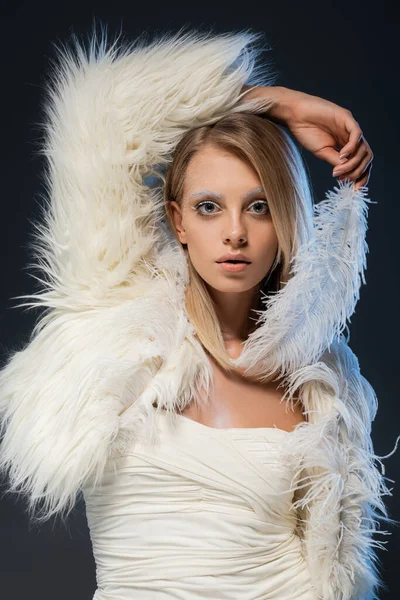 Красивая молодая женщина в искусственном меховом пиджаке смотрит в камеру, позируя с белым пером, изолированным на голубом — стоковое фото
