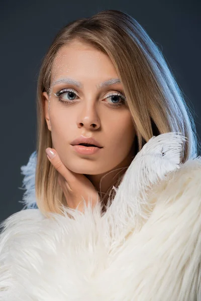 Bonita mujer joven en invierno chaqueta de piel sintética mirando hacia otro lado aislado en azul - foto de stock