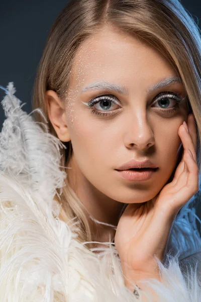 Retrato de jovem mulher em casaco de pele falso posando com pena branca isolada em azul escuro — Fotografia de Stock