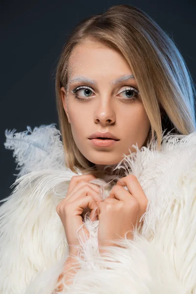 Retrato de jovem loira em casaco de pele falso posando com penas brancas isoladas em azul — Fotografia de Stock