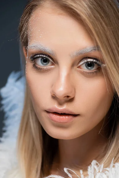 Portrait of pretty young woman looking at camera while posing near white feather isolated on blue — Stock Photo