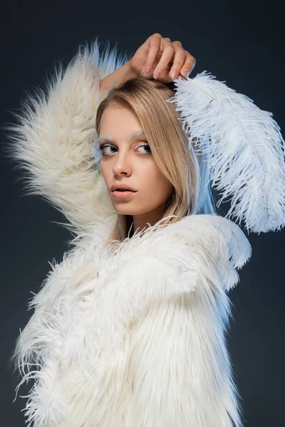 Young blonde woman with winter makeup looking away and posing with feather isolated on blue — Stock Photo