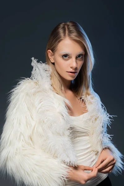 Mujer joven en chaqueta de piel sintética con plumas blancas de pie aislado en azul — Stock Photo