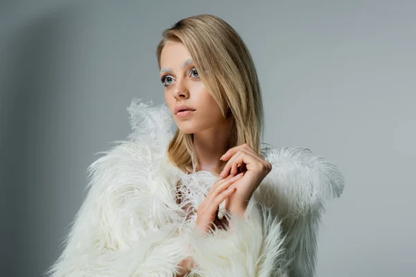 Young woman in faux fur jacket with white feathers looking away on grey — Stock Photo