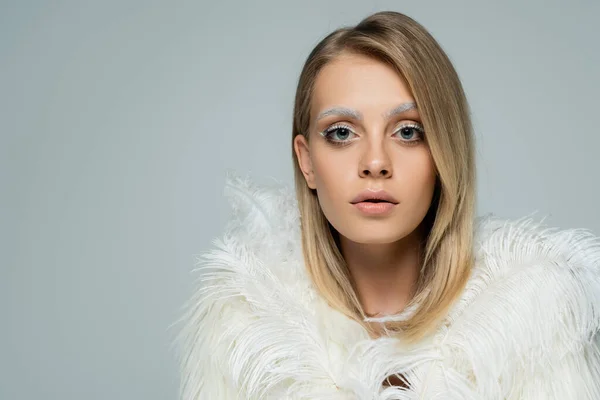 Young model in faux fur jacket with white feathers looking at camera isolated on grey — Stock Photo