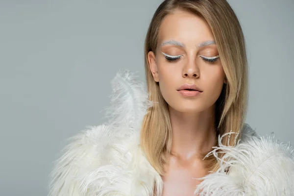 Junge Frau mit Winter-Make-up posiert mit geschlossenen Augen in stylischer Kunstpelzjacke mit weißen Federn isoliert auf grau — Stockfoto