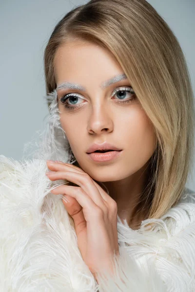 Portrait of young woman with winter makeup and white eyebrows posing near white feather isolated on grey — Stock Photo