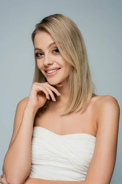 Femme blonde heureuse avec les épaules nues et le maquillage naturel en regardant la caméra isolée sur gris — Photo de stock