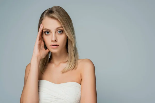 Mujer concentrada con hombros desnudos y maquillaje natural mirando a la cámara aislada en gris - foto de stock