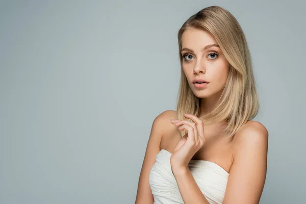 Blonde woman with bare shoulders and natural makeup looking at camera isolated on grey — Stock Photo