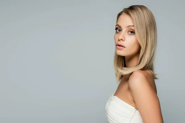 Jeune femme blonde avec maquillage naturel regardant la caméra isolée sur gris — Photo de stock