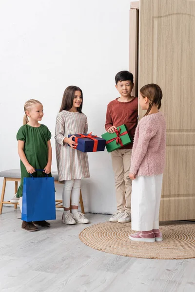 Веселі міжрасові діти тримають подарунки біля друга і дверей вдома — стокове фото