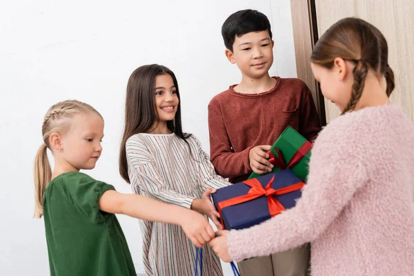 Niños multiétnicos dando regalos a un amigo borroso en casa - foto de stock