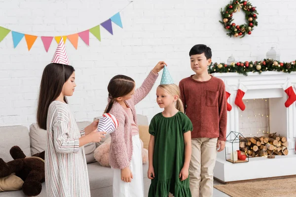 Interracial kids holding party caps during birthday party and christmas at home — Stock Photo