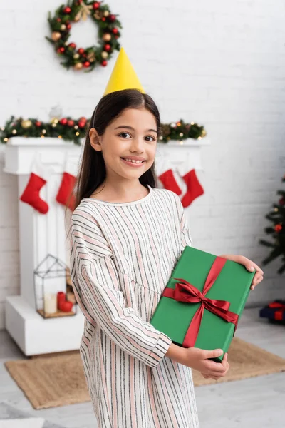 Retrato de menina alegre no tampão do partido segurando caixa de presente durante a festa de aniversário no inverno — Fotografia de Stock