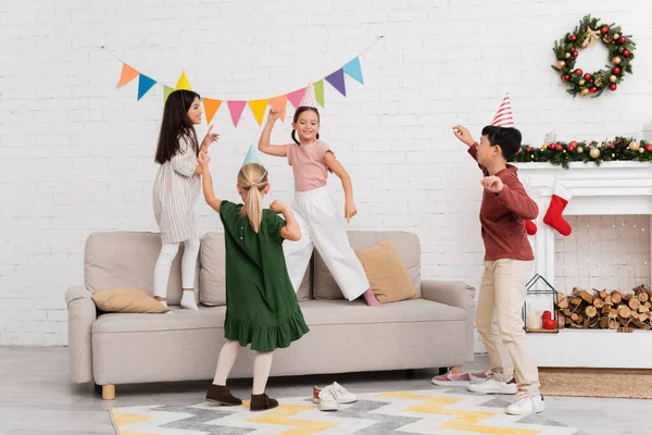 Positive multiethnische Kinder spielen Tag in der Nähe von Weihnachtsdekoration im Wohnzimmer — Stockfoto