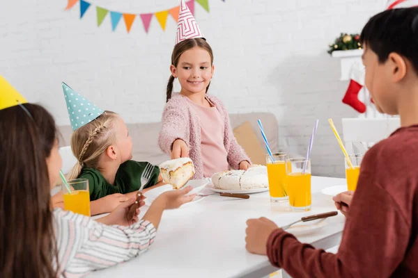 Bambino allegro in berretto di partito che dà la torta di compleanno ad amico durante celebrazione a casa — Foto stock