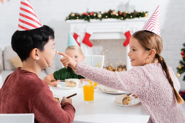 Smiling girl smearing nose of asian friend with cream during birthday party at home — Stock Photo