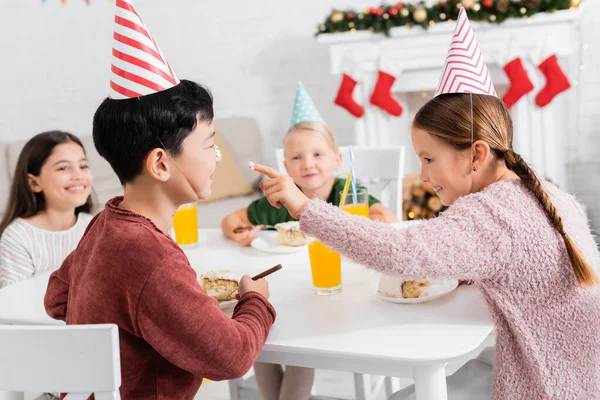 Niño celebración pastel crema en dedo cerca asiático amigo durante cumpleaños celebración en casa - foto de stock