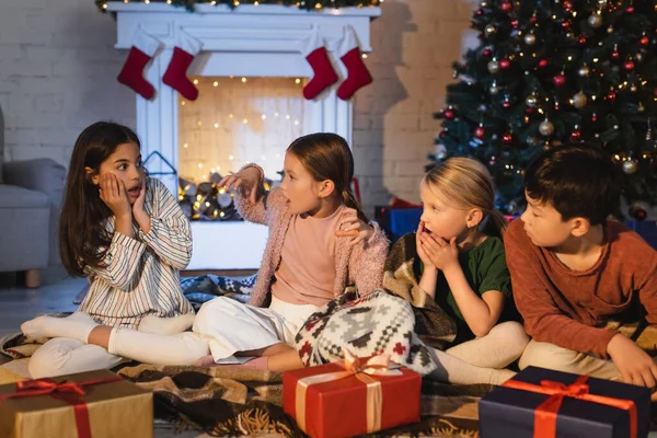 Ragazza spaventata seduta vicino ad amici multietnici e regali durante la celebrazione di Natale a casa — Foto stock