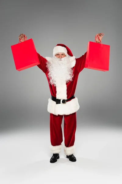 Full length of father christmas holding shopping bags on grey background — Stock Photo