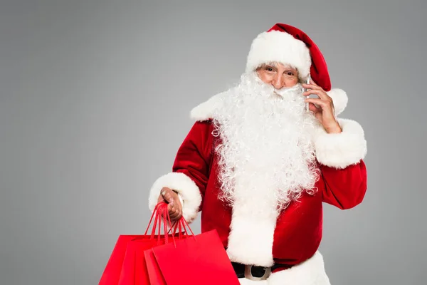 Father christmas talking on smartphone and holding shopping bags isolated on grey — Stock Photo