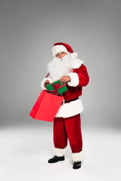 Weihnachtsmann legt Geschenk mit Schleife in Einkaufstasche auf grauem Hintergrund — Stockfoto